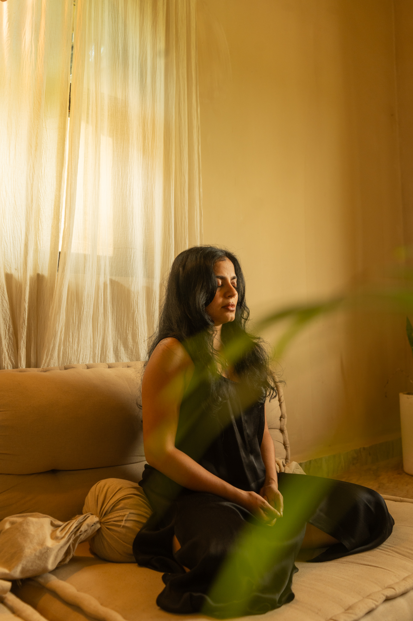 Alisha Netalkar seated in stillness beside a sunlit curtain