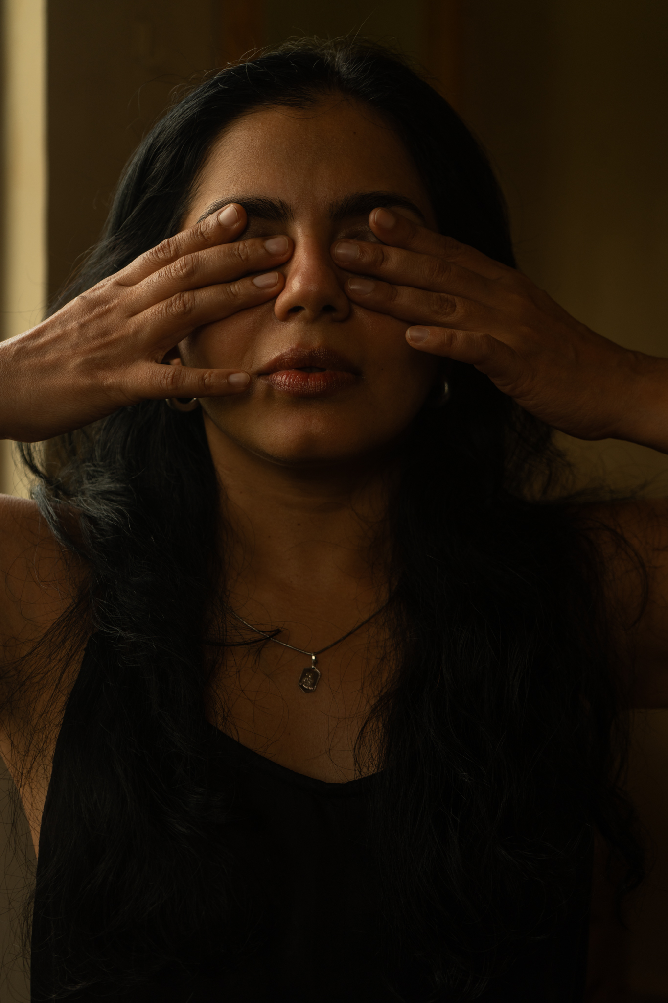 Portrait with hands resting over closed eyes in low light