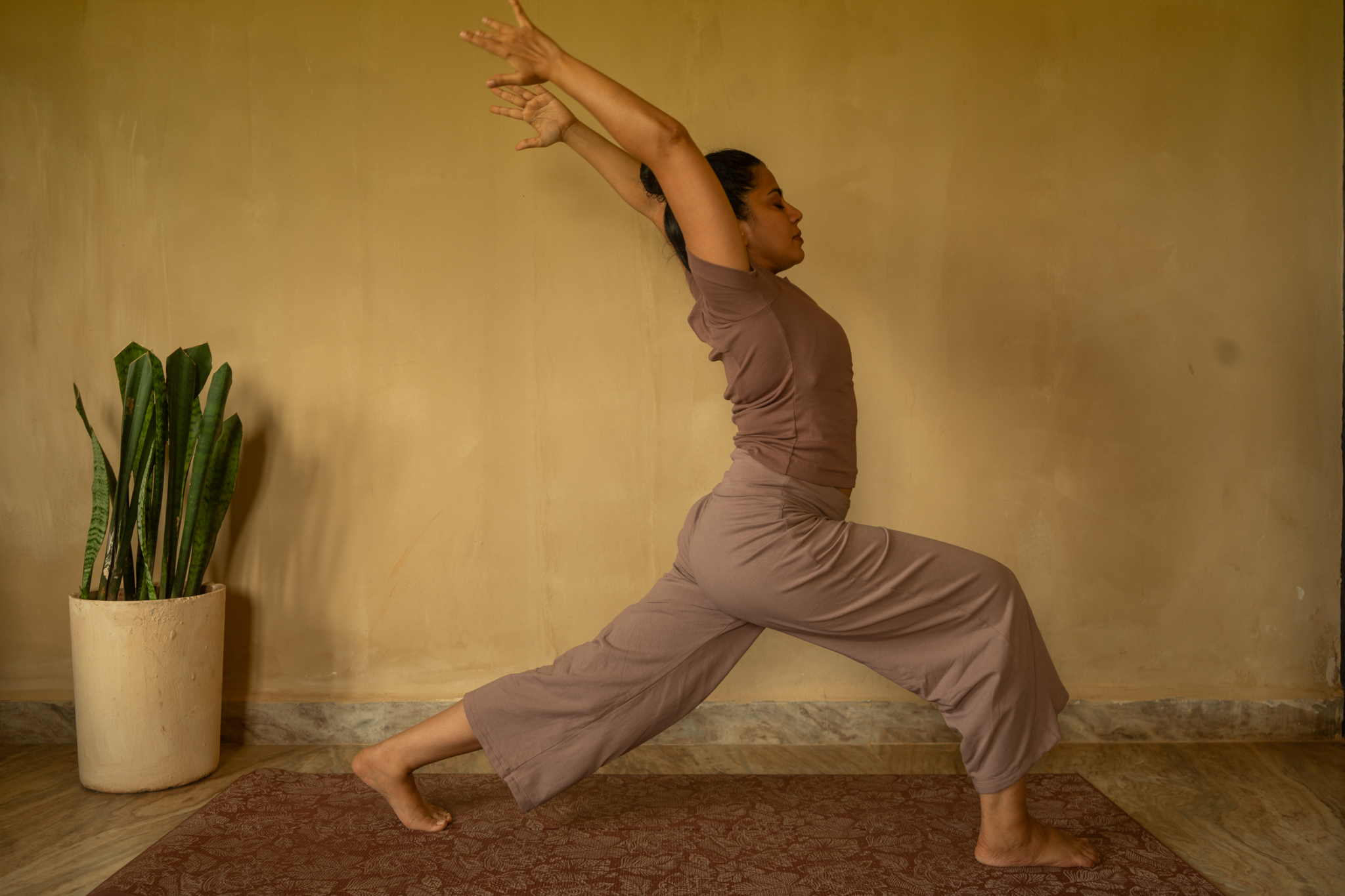 Alisha Netalkar in a standing yoga posture against an ochre wall